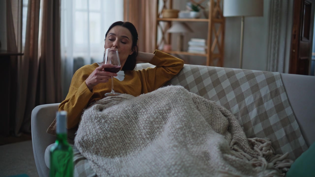 Donna con il cuore spezzato che si rilassa sul divano, tenendo un bicchiere di vino. Donna seria che beve vino.
