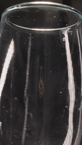 transparent champagne wineglass with stains turning on dark background. empty glassware for alcohol drink on table reflecting bright light macro