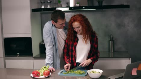 Pareja-Divertida-Cocinando-Juntos-En-Una-Cocina-De-Color-Gris,-Familia-Joven-Y-Activa-Divirtiéndose,-Riendo-Y-Sin-Preocupaciones.-Hombre-Feliz