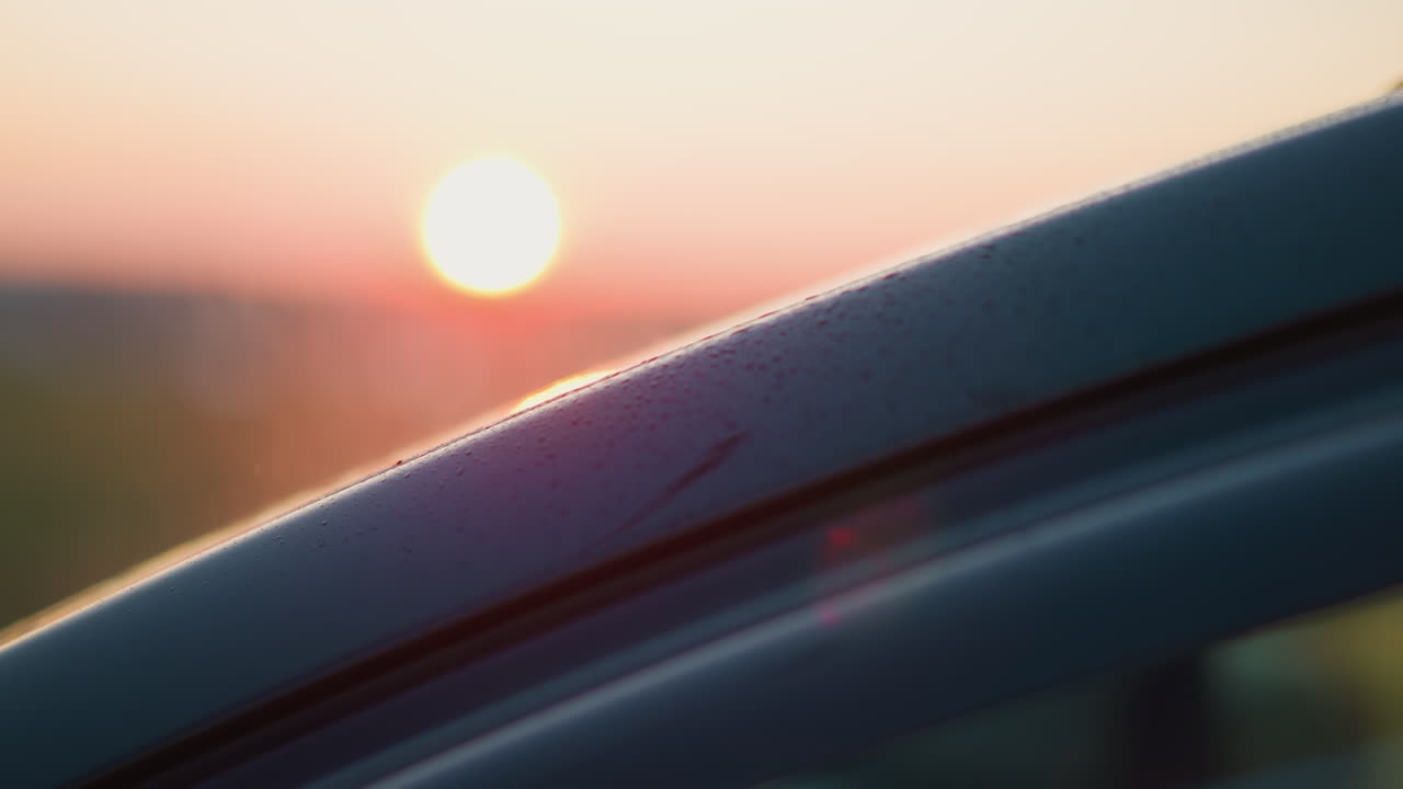 일몰 때 비가 내리는 자동차 근접 사진 자동차 지붕은 강한 비가 내리면 물방울로 여 있습니다.