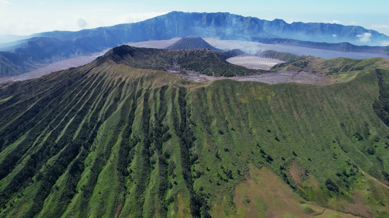 Cinematic drone pullback of Mount Bromo smoking with Mount Batok and the full Tengger caldera revealed. Stunning aerial view from the north side in East Java, Indonesia