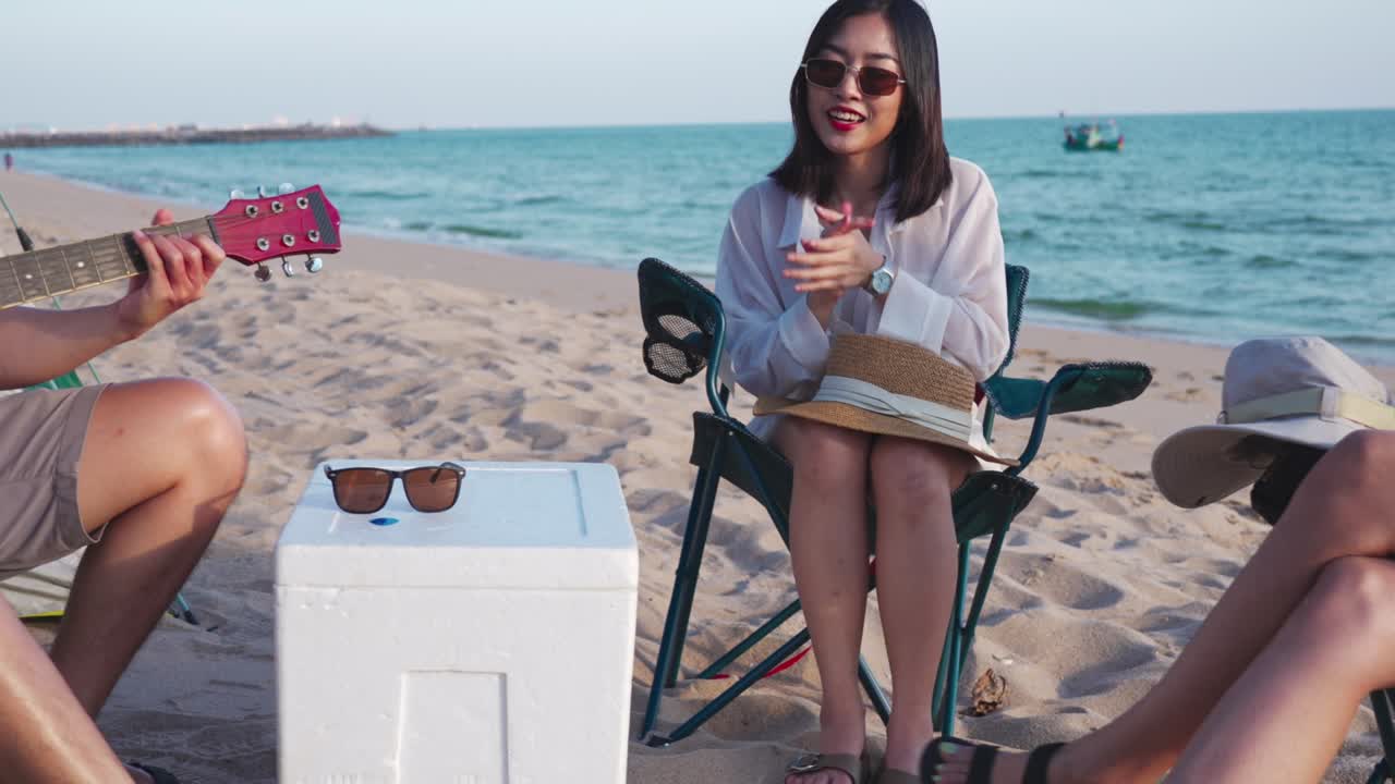 jóvenes felices disfrutando con música en la playa, joven tocando la guitarra y cantando como sus amigos aplaudiendo y riendo, divirtiéndose en la playa picnic en vacaciones de verano, vacaciones.