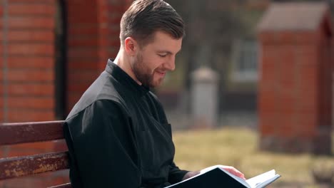 closeup portrait of a reading priest sitting on a bench