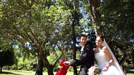 recién casados felices montando un scooter rojo en el parque