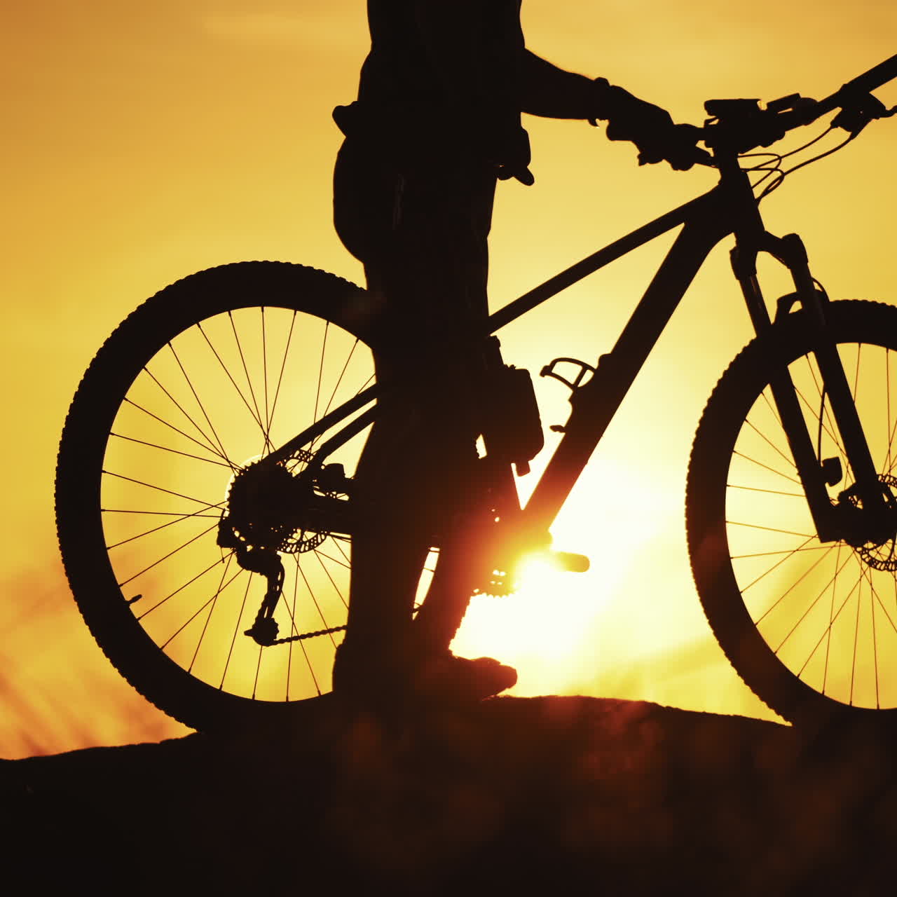 Sportsman biker walk with bike outdoors at golden sunset. Silhouette of a bicycle and a cyclist walking in the evening against the beautiful summer sunset. Close-up.