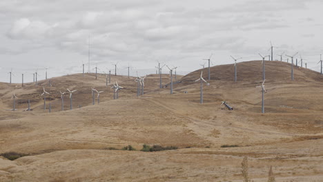 a large group of windmills not turning, some broken, on dry hill on cloudy day