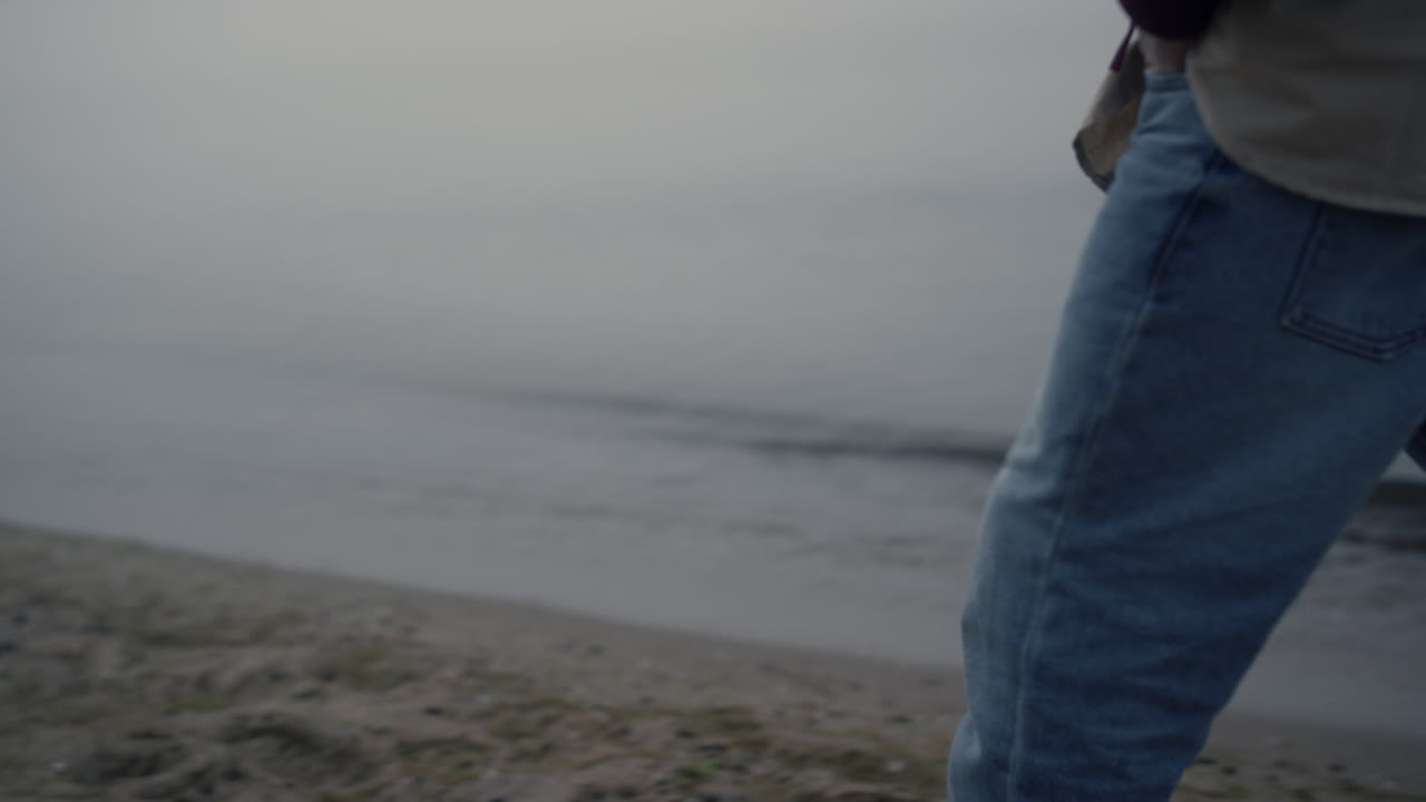 Uomo irriconoscibile che cammina sulla spiaggia. Ragazzo con le mani nelle tasche dei jeans in primo piano.