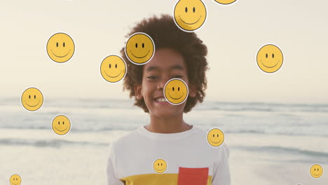 animación de iconos emoji sobre un niño afroamericano feliz en una playa soleada