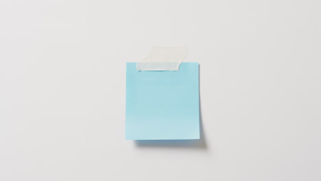 Video-of-close-up-of-blue-memo-note-with-copy-space-taped-to-white-background