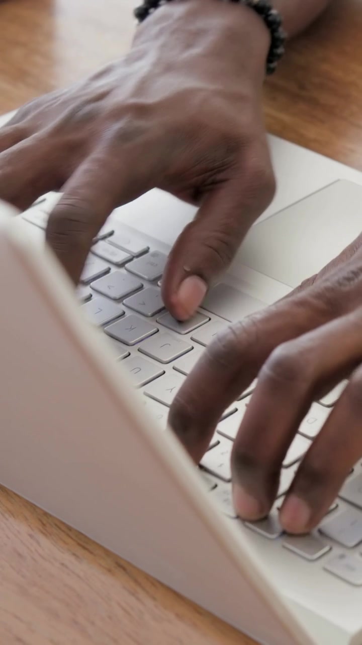 Vertical video: Preparing hands moving into view then typing at desk, working on laptop with watch
