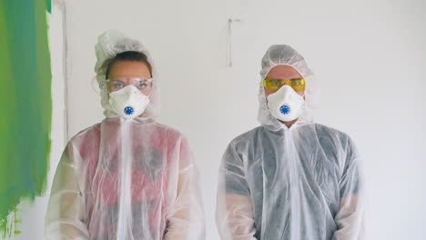 young family in protective suits holds rollers near wall