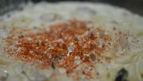 close up view of spices being sprinkled onto bubbling macaroni pasta in cream sauce