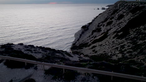 Twilight-view-over-the-serene-waters-near-Aphrodite's-Rock-in-Paphos,-with-the-rocky-coastline-silhouetted-against-the-calm-sea