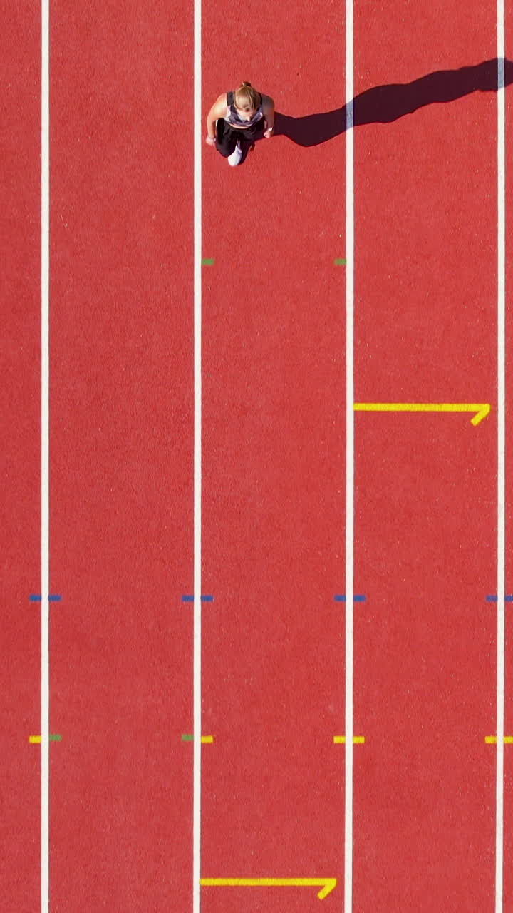 Top down vertical view of a female athlete sprinting on a red running track at a stadium. Perfect for fitness apps, sports marketing, and social media reels