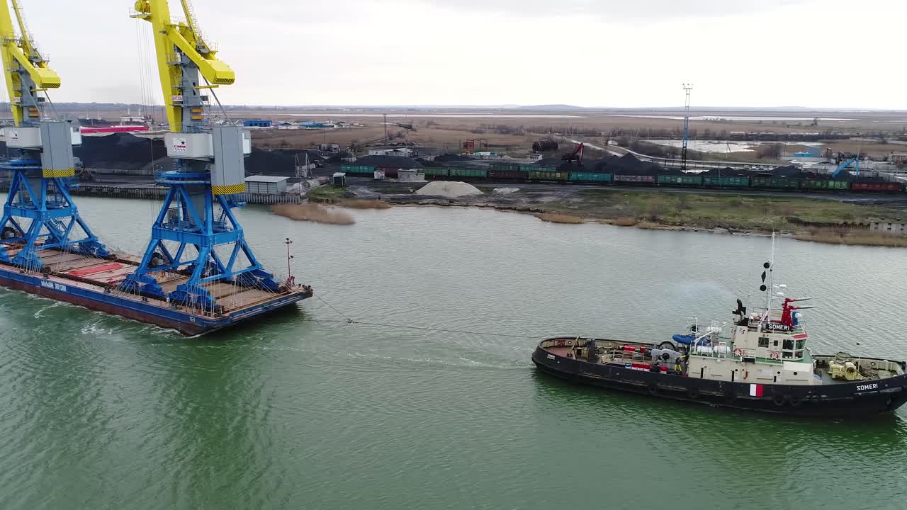 remolcador que asiste a una barcaza en el puerto con una grúa