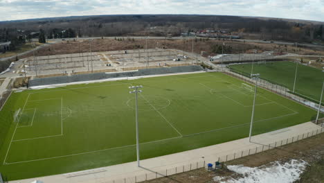 drone view of empty soccer field during winter as the snow is thawing with parking lot and road in the distance