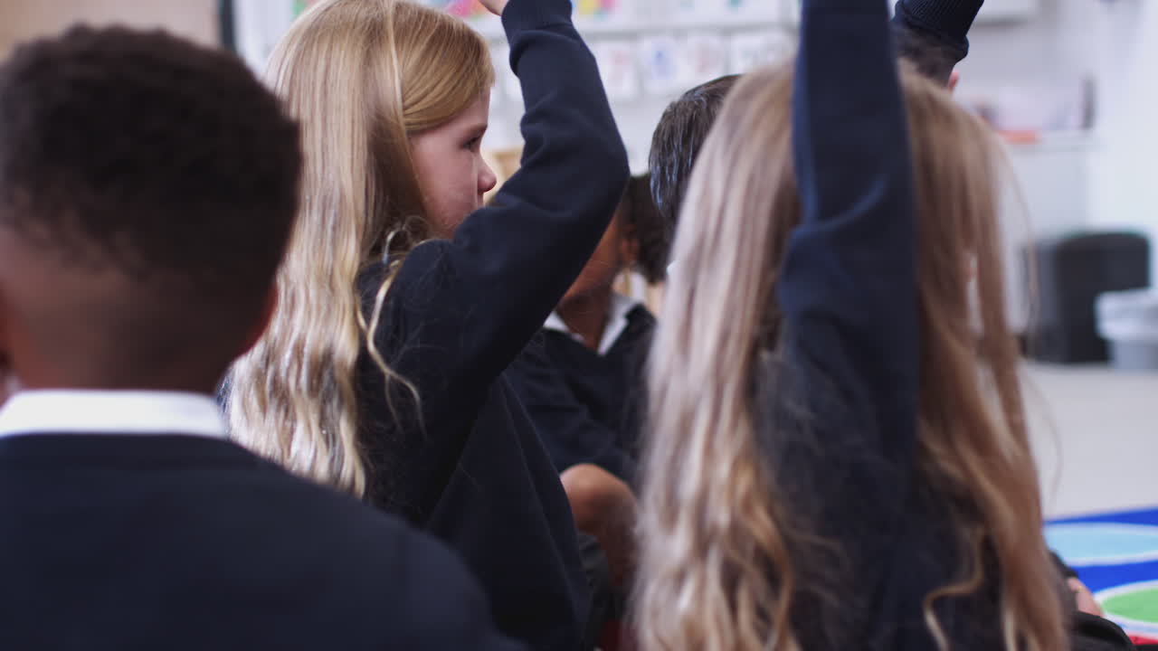 niños de la escuela primaria sentados en un aula levantando las manos para responder a una pregunta, enfoque selectivo