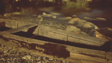 old wooden boat rests by the riverbank surrounded by stones and greenery