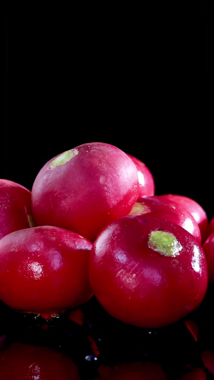 A group of glossy red radishes rotates smoothly on a reflective black surface under bright studio lighting, highlighting texture, color, and freshness in high resolution
