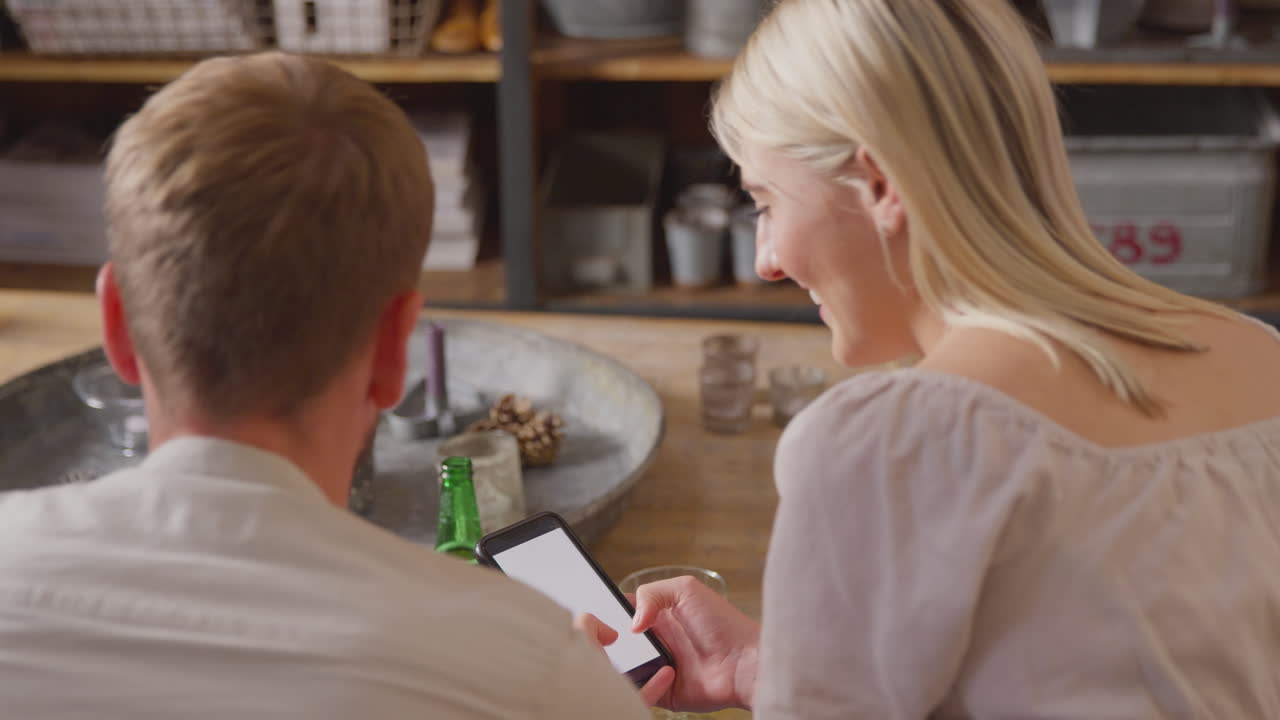 집 에서 휴대 전화 를 함께 보고 있는 소파 에 앉아 있는 친구 들 의 뒤쪽 전망