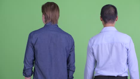 two businessman looking excited and happy with arms raised against green studio background