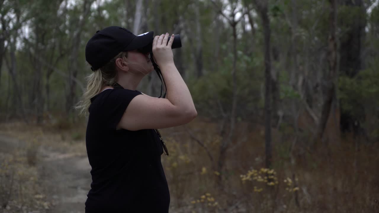 chica rubia con sombrero mirando a través de binoculares en la naturaleza