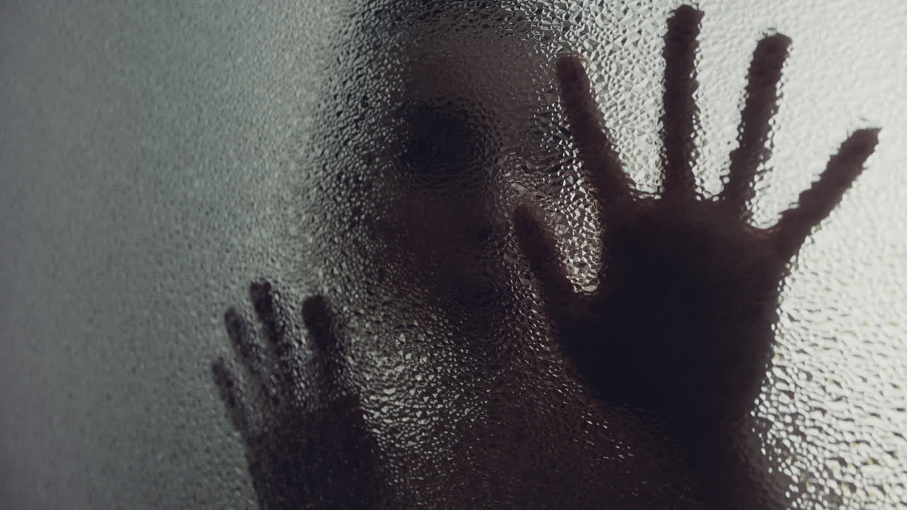 A female silhouette behind the frosted window touches the glass slowly