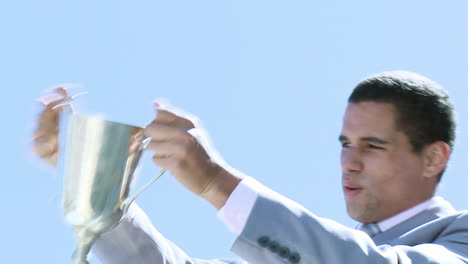 un hombre de negocios feliz sosteniendo un trofeo al aire libre.