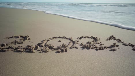 Year-2021-written-in-the-sand-at-the-beach-is-partially-getting-washed-away-by-a-sea-wave