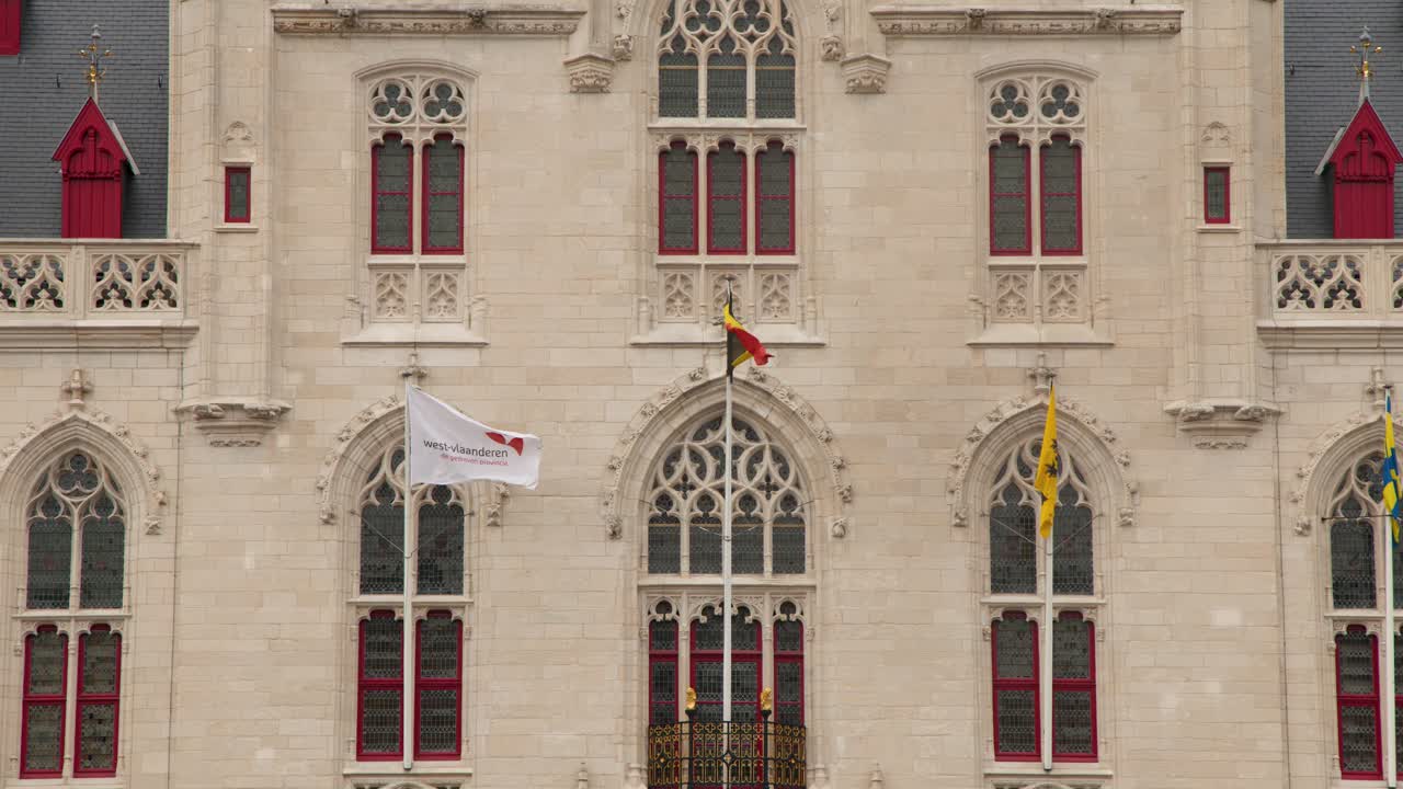 Static shot of Bruges city hall facade with waving flags, overcast daylight, symmetrical composition
