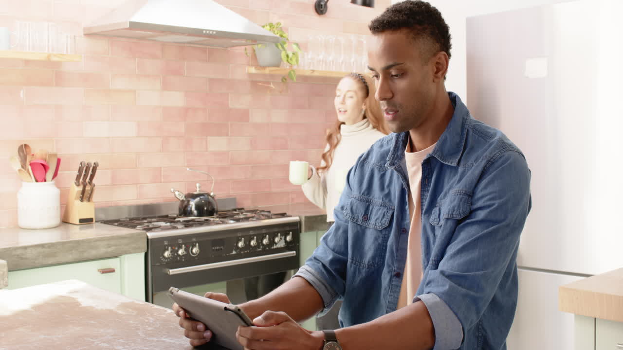 Couple in kitchen enjoying coffee and looking at tablet, surprised and happy