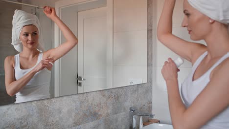 Caucasian-woman-with-towel-on-hair-applying-antiperspirant.