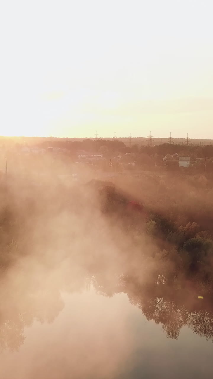 smoke from the fire are spreading over the river at sunset on the background of a power station with two pipes. Aerial view Vertical video
