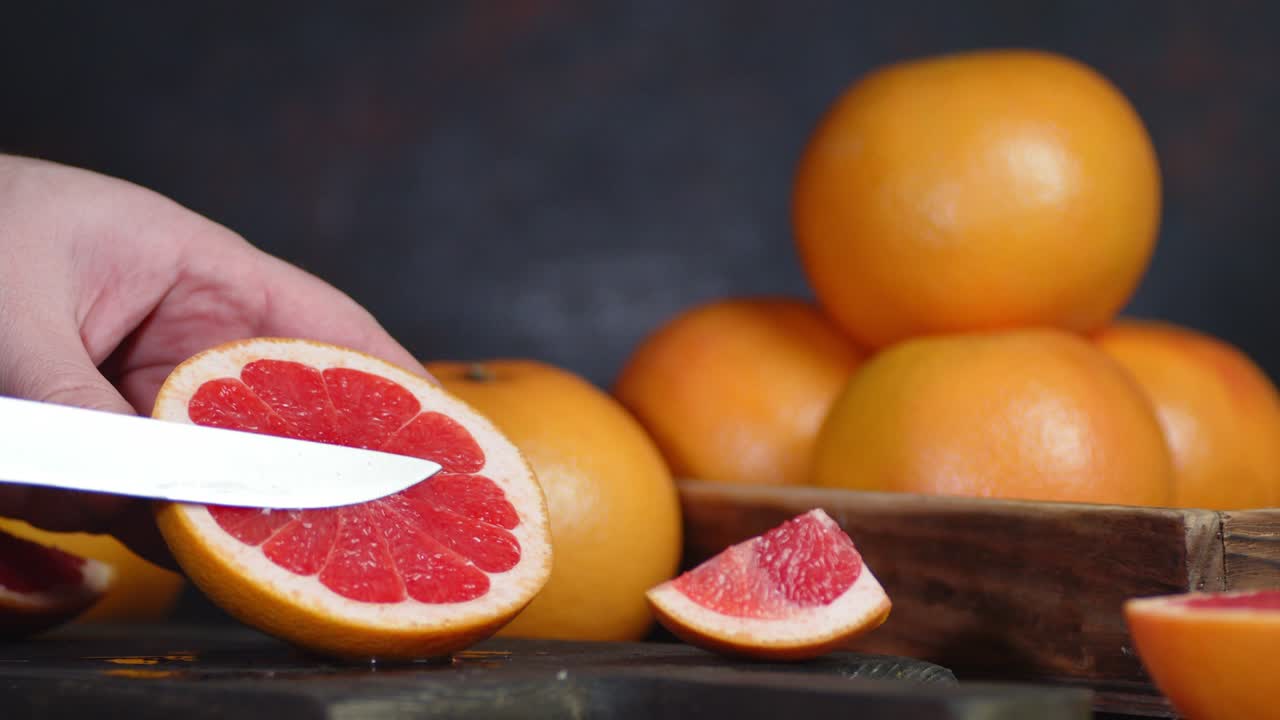 Male hand with a knife squeeze the juice of ripe grapefruit.