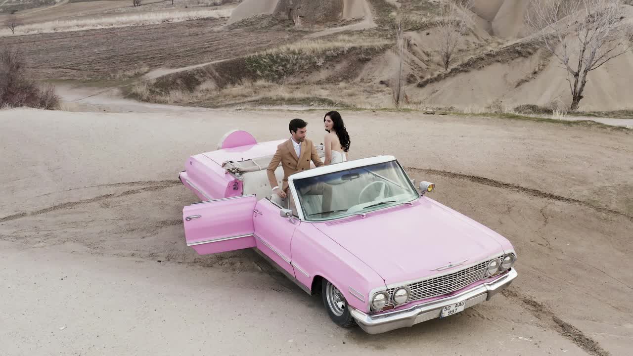 una pareja en un coche descapotable rosa en un paisaje pintoresco
