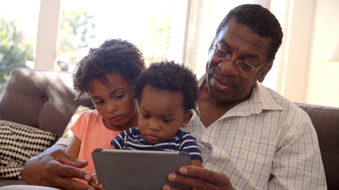 Nonno e nipoti a casa che usano un tablet digitale.