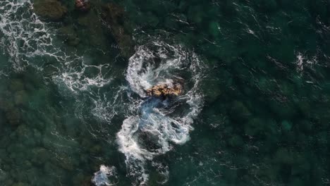 aerial view of waves crashing on rocks in turquoise ocean