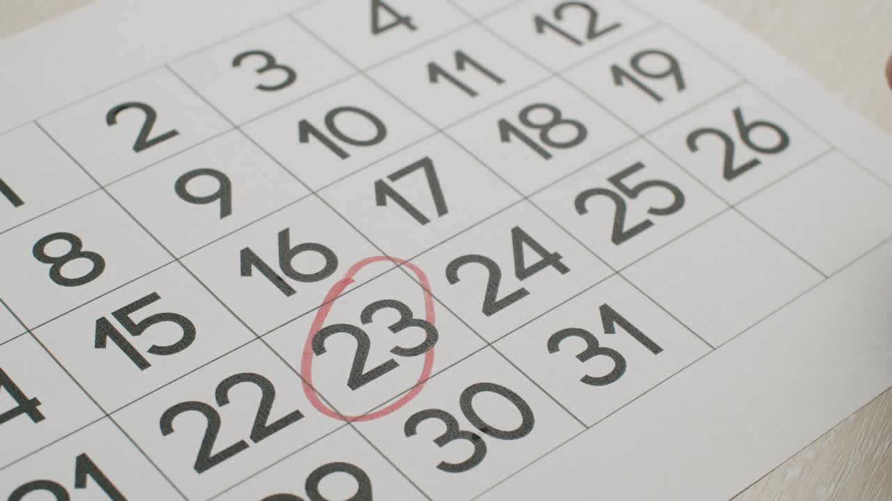 la mano del hombre escriba el día 23 en el calendario de papel usando un bolígrafo rojo.
