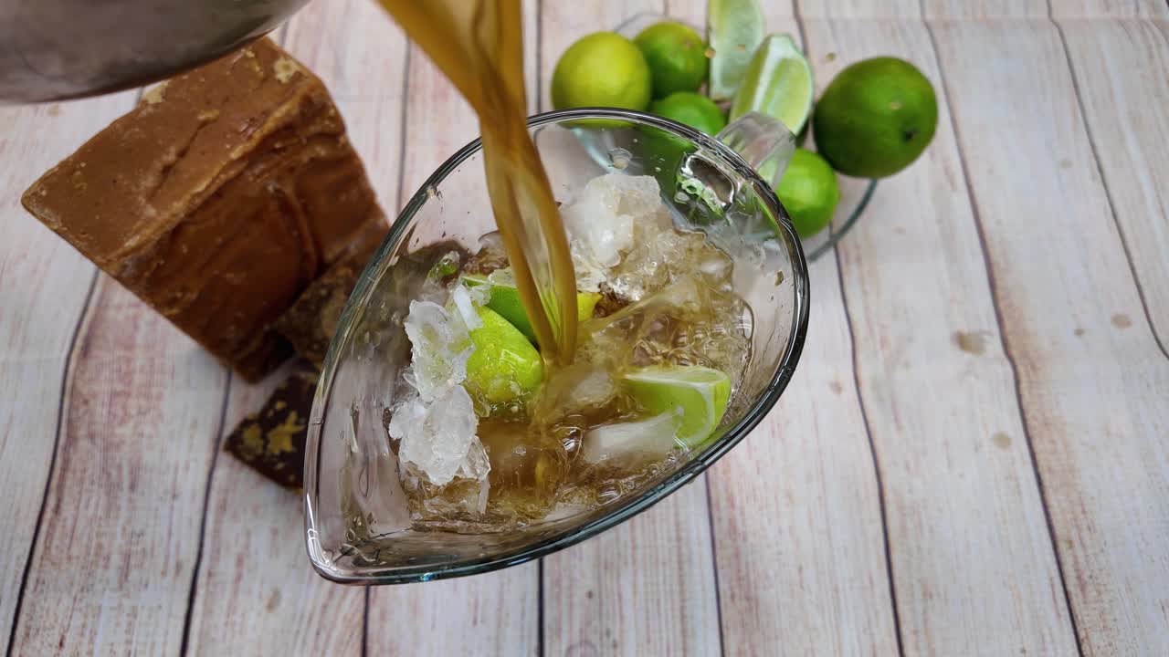 Versare sciroppo di panela dorato in una brocca con ghiaccio e lime per una bevanda