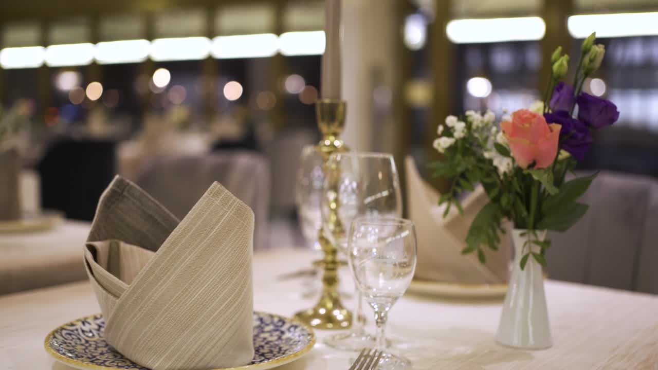 Footage of a nicely decorated dinner table in a luxurios nice restaurant, with some nice flowers, dishes and a candle.