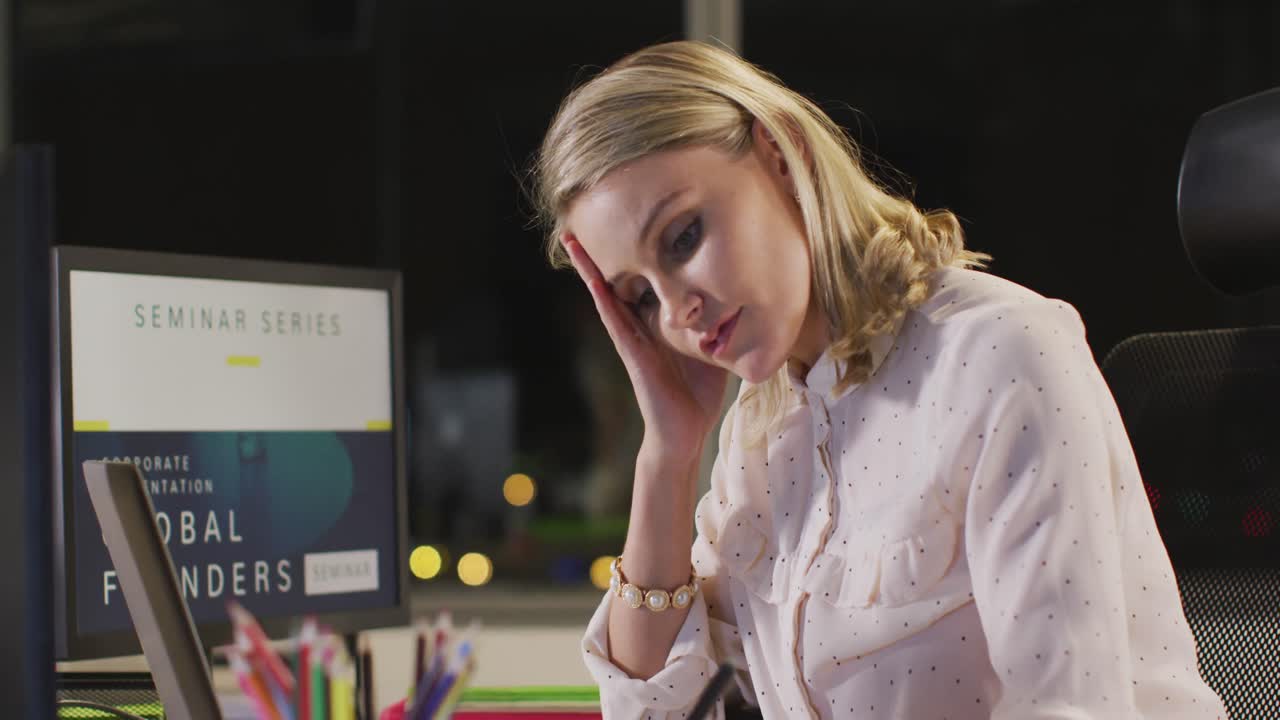 Tired professional businesswoman making notes while looking at her laptop screen in modern office