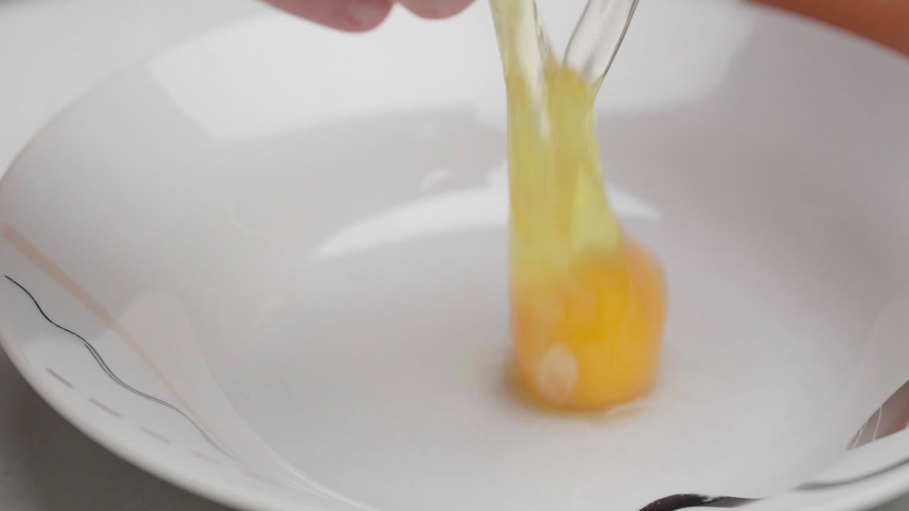 Rallentatore ravvicinato di un uovo che viene rotto e fatto cadere in una ciotola bianca
