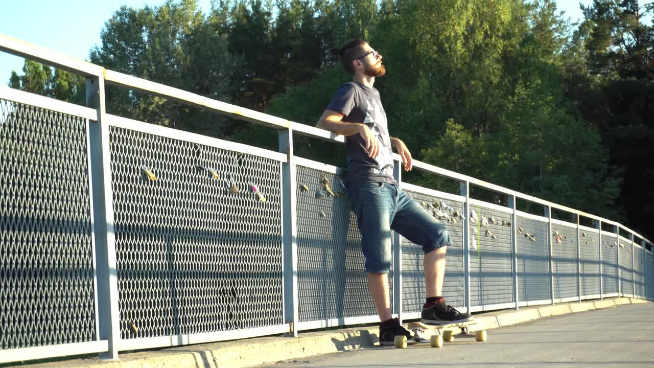 Young male man is standing on the long board on the bridge catching sun light