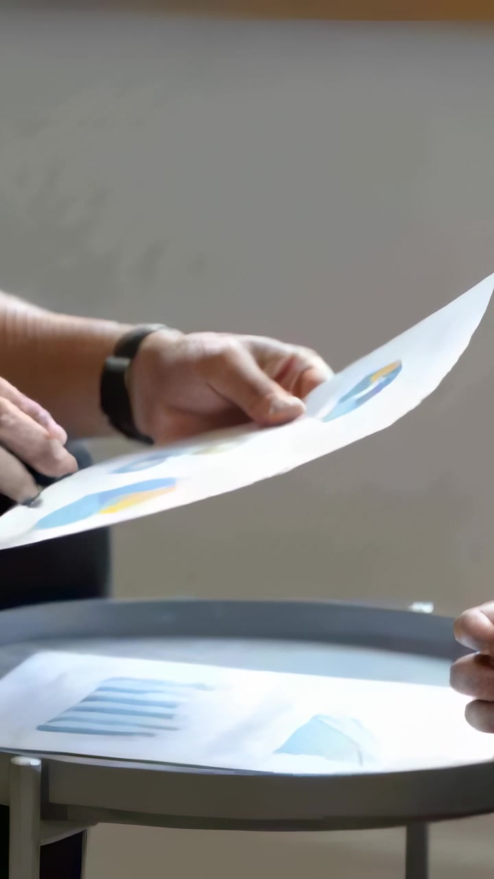 Vertical video: Tilting paper, holder in dark short-sleeve passing pie charts during work review
