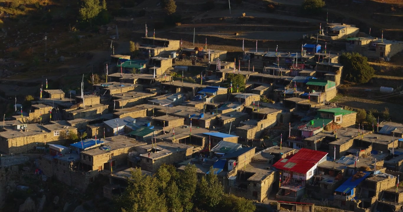 Circuito dell'Annapurna, Manang, Nepal, ripresa aerea in movimento su dense case in pietra, chorten buddisti e bandiere di preghiera in un villaggio di montagna durante le prime ore del mattino.