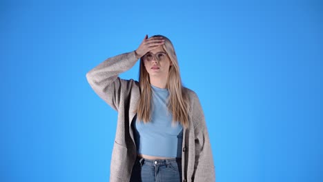 sick woman checks forehead for fever and sneezes into tissue, blue background