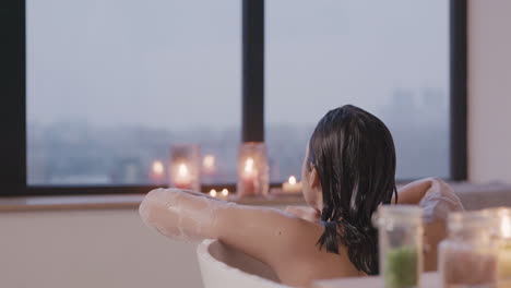 rear view of a woman taking a bath in a bathtub while looking out the window, then looking at side