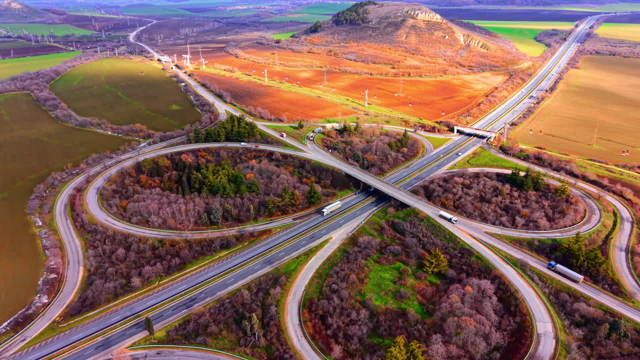アスファルトの道に車両が見える道路のインターチェンジ。紅葉した木々と農地に囲まれた、対称的な高速道路のクローバー型インターチェンジ。
