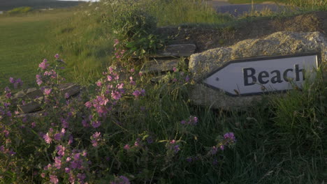 Close-up-of-sign-on-stone-wall-directing-the-way-to-British-beach,-panning-shot