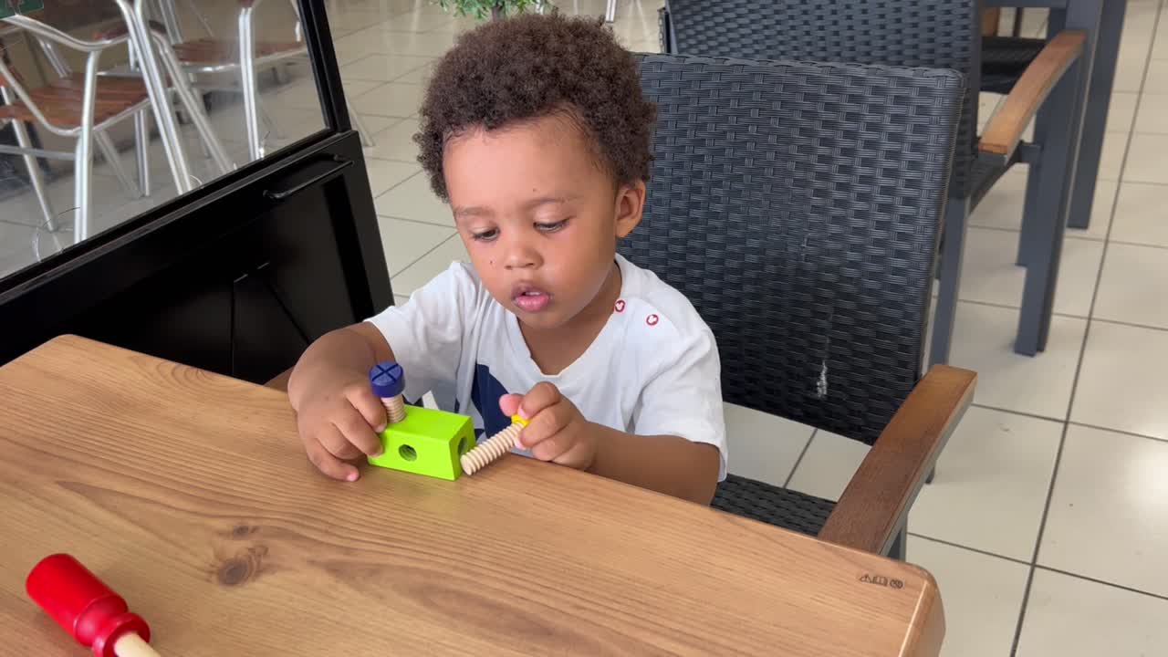 Lovely and cute two year old afro european child playing with some toy tools seated on a table